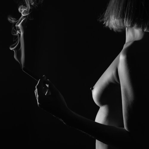 Un cigare à la main, les volutes de fumée tourbillonnants, elle se tient dans la lumière qui fait apparaitre sa nudité.