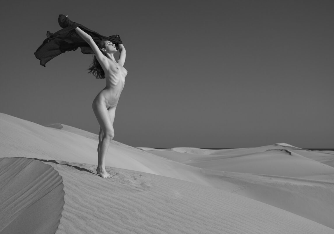 Sous le vent , le tissu et les cheveux de la modèle. Corps nu au soleil, sur une dune de sable.