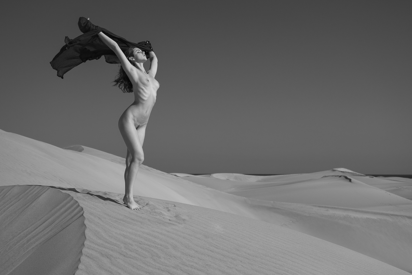 Sous le vent , le tissu et les cheveux de la modèle. Corps nu au soleil, sur une dune de sable.