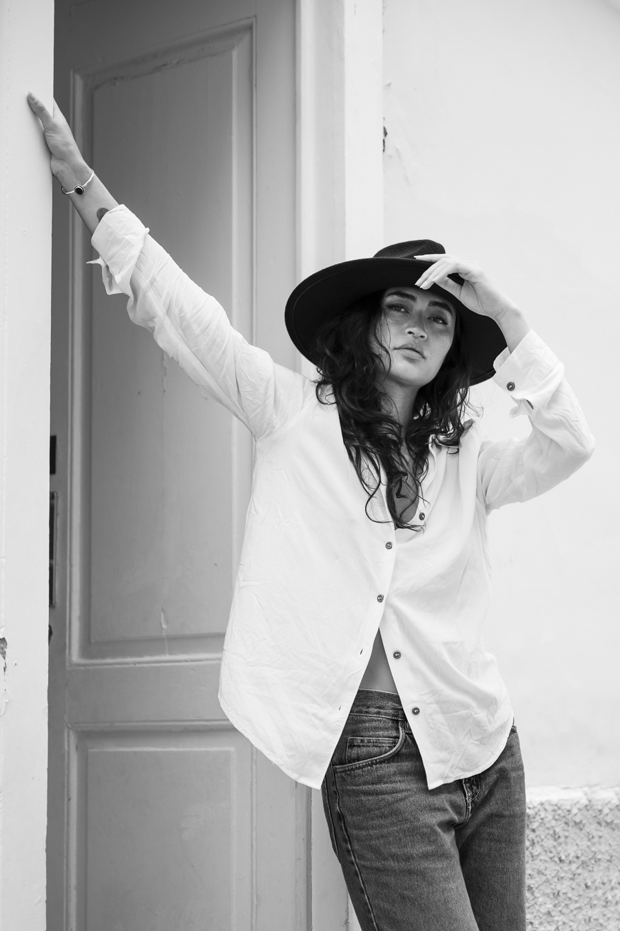 Image en ville, devant un cadre de porte. Chapeau, chemise blanche, la modèle regardant l'objectif