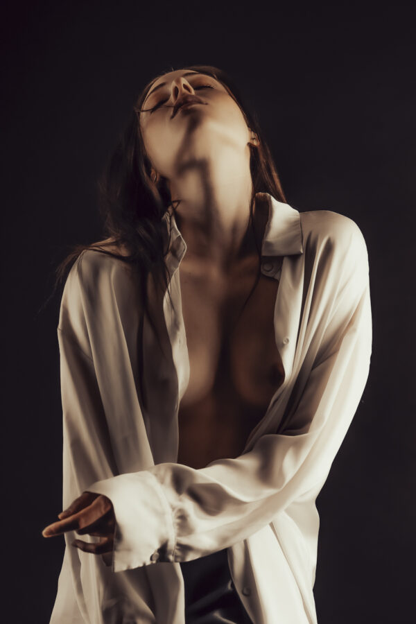 chemise ouverte sur la peau nue, tête inclinée en arrière, une pose travaillée et sensuelle. Image en couleur.