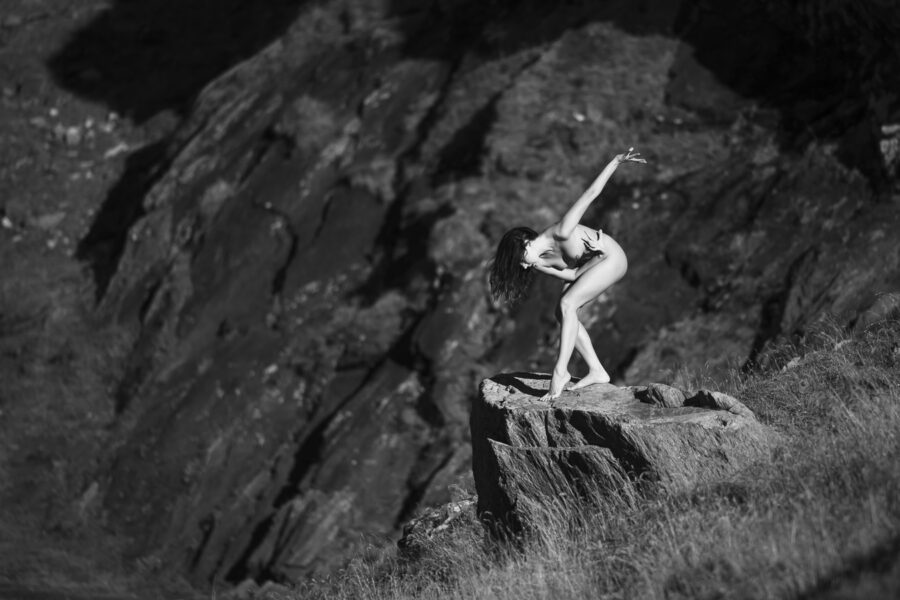 Au bord de l'eau, debout sur un rocher, les lignes du corps se détachent sur le fond gris de la montagne