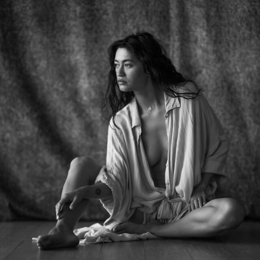 Noir et blanc en studio, la modèle assise au sol porte une tenue ample décontractée.